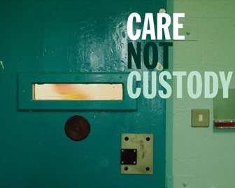 A door of a prison cell with the words "Care not Custody" written over it