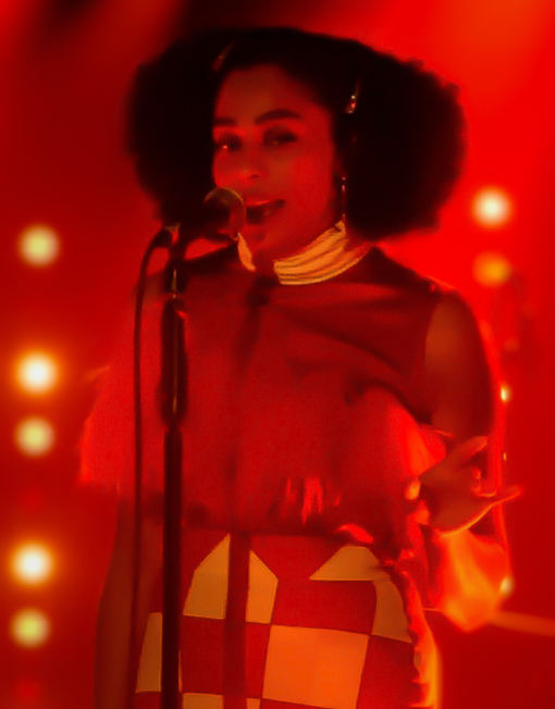 Celeste standing behind a microphone, singing in a room filled with red lighting