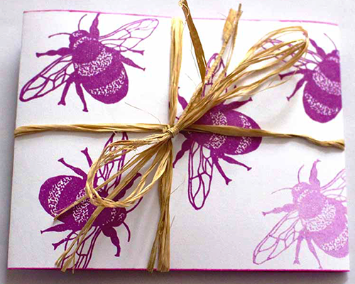 A white paper folder decorated with purple bumble bees and tied with brown raffia
