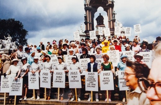 A group of WI members standing outside holding signs with different WI resolutions written on them