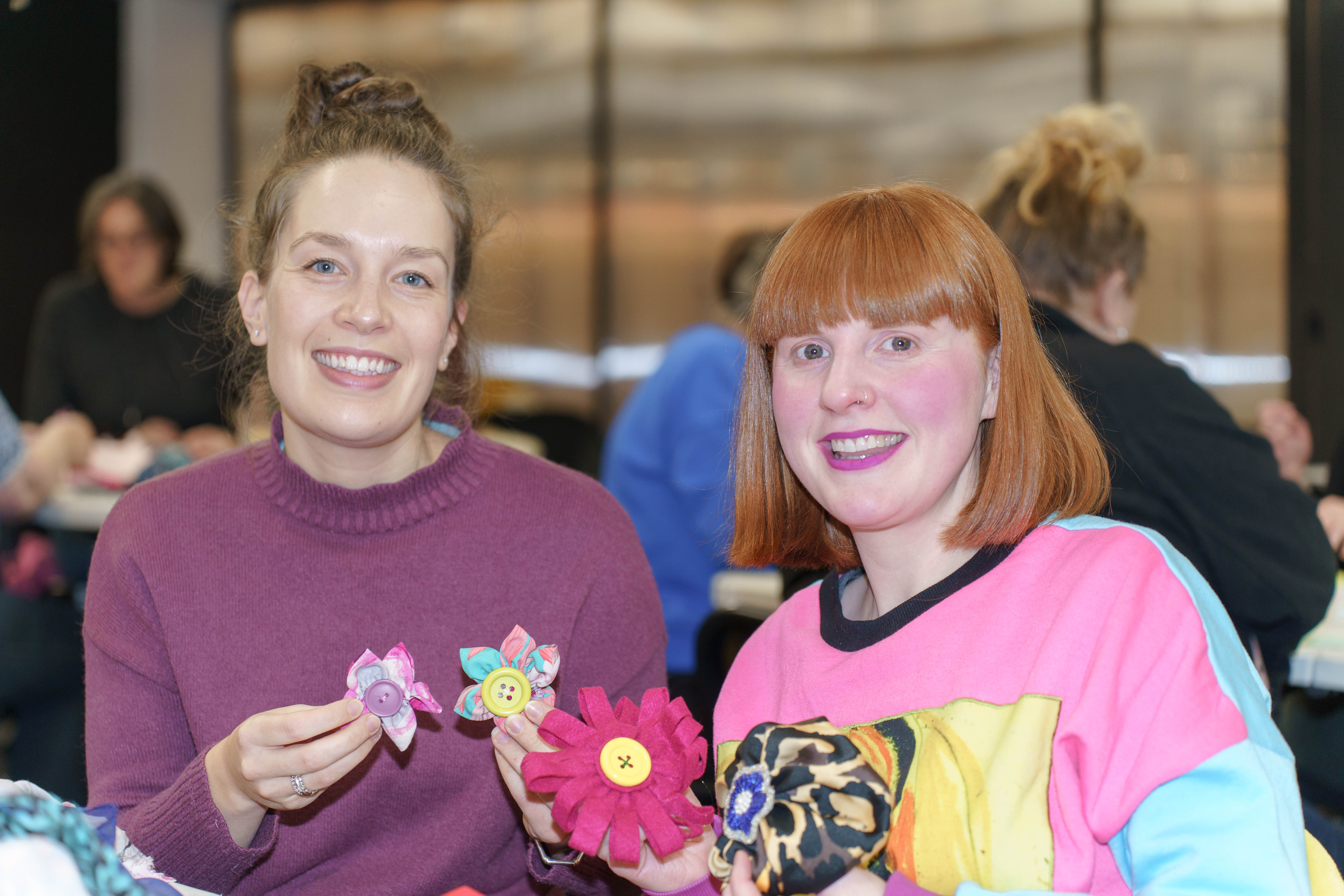 Two women smiling holding crafted flowers.