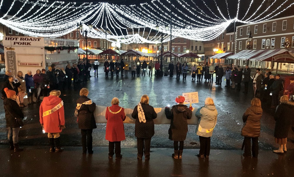 A large group of women standing outside at an event/protest held at a Christmas Market