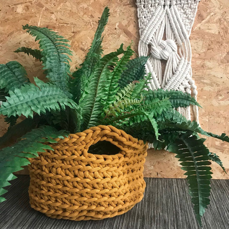 A brown crochet basket with a plant inside