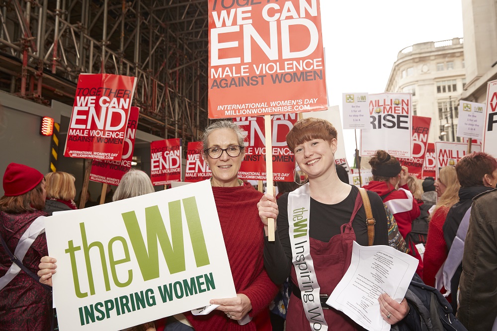 Two women at the Million Women Rise march holding up a WI logo and a placard